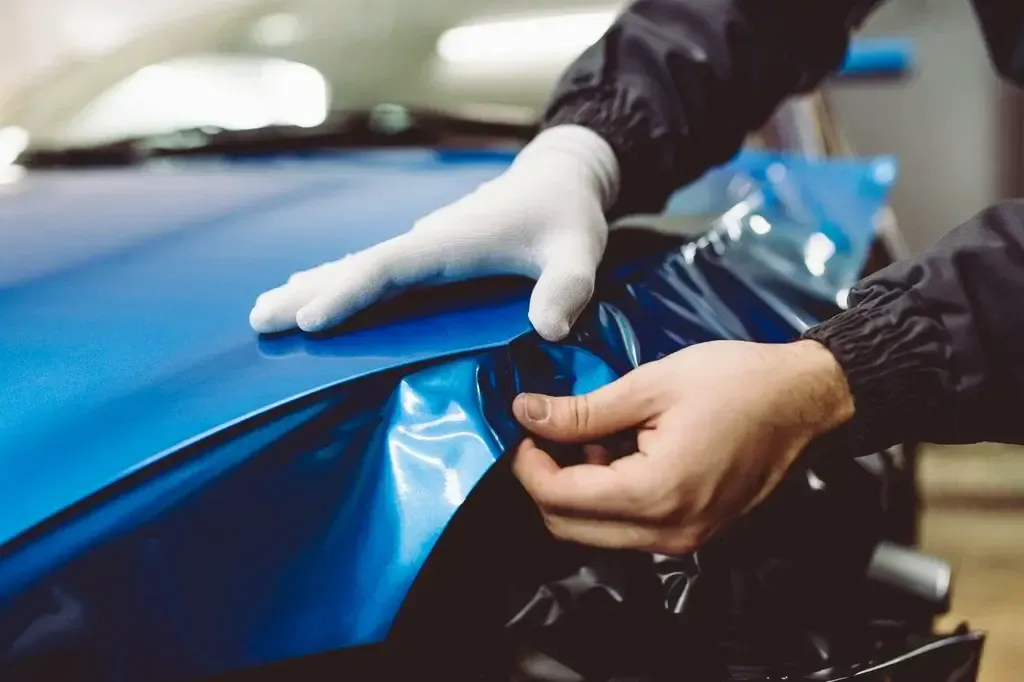 Técnico con guantes instalando vinil azul brillante sobre el cofre de un vehículo.