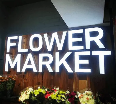 Letrero iluminado 'Flower Market' sobre exhibición de flores.