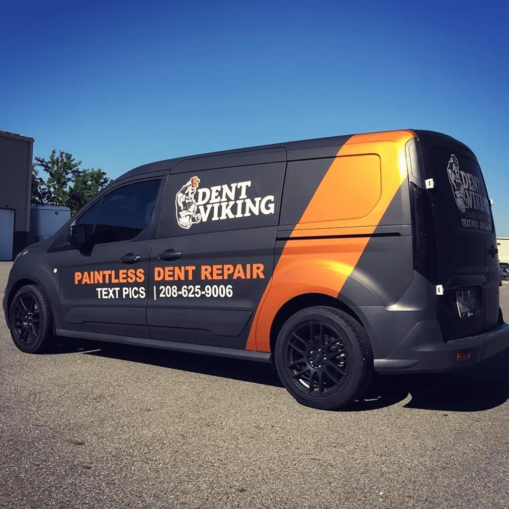 Van negra con wrap naranja y logos Dent Viking estacionada al exterior.