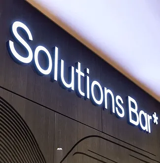 Letrero iluminado de 'Solutions Bar' sobre pared de madera oscura.