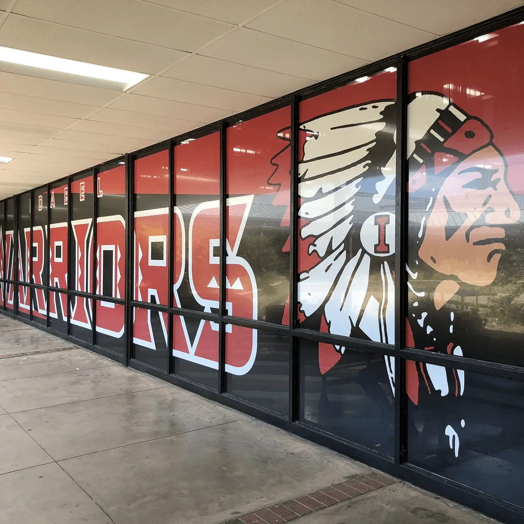 Fachada de tienda con gráficos de guerrero y textos en vinil perforado sobre ventanales.
