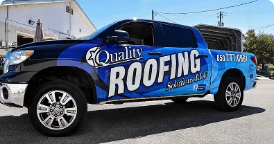 Pickup negra con wrap azul y blanco de Quality Roofing estacionada en calle, vista lateral.